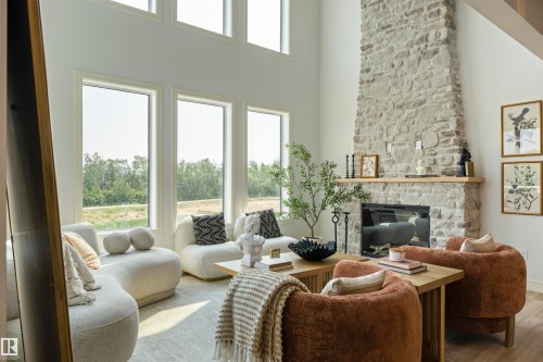 Living space featuring a tall stone fireplace with a wood mantel, multiple large windows, and a high ceiling - 3329 Chickadee Drive, Edmonton, AB 