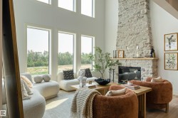 Living space featuring a tall stone fireplace with a wood mantel, multiple large windows, and a high ceiling - 