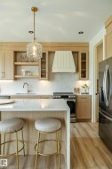 Kitchen featuring light wood-finish cabinetry, a waterfall-edge island with a light-toned countertop, and stainless steel appliances - 