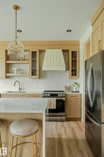 Modern kitchen featuring light wood-finish cabinetry, a stainless steel range with a custom range hood, and light-toned countertops - 3329 Chickadee Drive, Edmonton, AB 