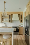 Modern kitchen featuring light wood-finish cabinetry, a stainless steel range with a custom range hood, and light-toned countertops - 
