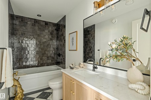 Bathroom featuring a white tub with dark subway tile surround, a light wood-finish vanity with a white countertop, a rectangular undermount sink, and matte black fixtures - 3329 Chickadee Drive, Edmonton, AB 