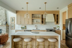 Open-concept kitchen featuring light wood-finish cabinetry, a large center island with a solid surface countertop, stainless steel appliances, and two decorative pendant lights - 