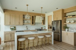 Contemporary kitchen featuring light wood-finish cabinetry, a large center island with a white countertop, stainless steel appliances, a white tile backsplash, and recessed lighting - 