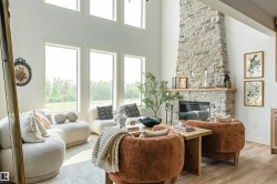 Spacious living area featuring a floor-to-ceiling stone fireplace with a wood mantel, high ceilings, large windows, and light wood-finish flooring - 