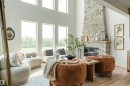 Spacious living area featuring a floor-to-ceiling stone fireplace with a wood mantel, high ceilings, large windows, and light wood-finish flooring - 3329 Chickadee Drive, Edmonton, AB 