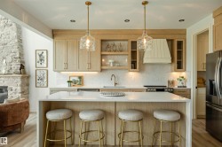 Gourmet kitchen featuring a central island with countertop seating, light wood-finish cabinetry, a built-in range hood, and stainless steel appliances - 