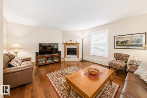 Living area featuring wood-finish flooring, a corner fireplace with a wood mantle, and a white-framed window with blinds - 512 3 Perron Street, St. Albert, AB 