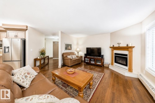 Spacious living area featuring wood-finish flooring, a corner fireplace with a wood mantle, and an open concept layout - 512 3 Perron Street, St. Albert, AB 