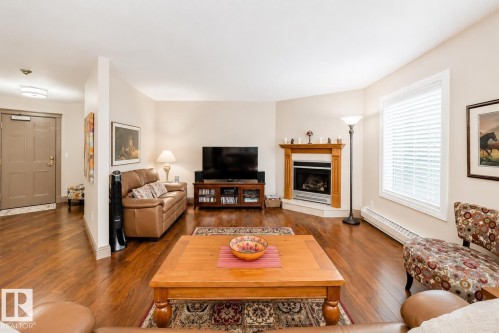 Spacious living area featuring wood-finish flooring, a corner fireplace with a wood mantel, and a large window with blinds - 512 3 Perron Street, St. Albert, AB 