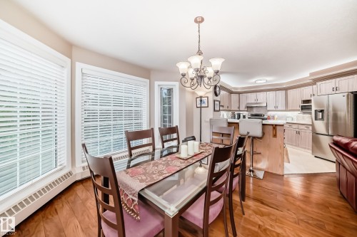 Dining area with wood-finish flooring, a glass-top dining table, and a multi-arm chandelier - 512 3 Perron Street, St. Albert, AB 
