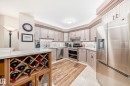 Contemporary kitchen featuring extensive light-toned cabinetry with crown molding, stainless steel appliances, a built-in wine rack, light-colored countertops, and mixed flooring with wood-finish planks and square tiles - 512 3 Perron Street, St. Albert, AB 