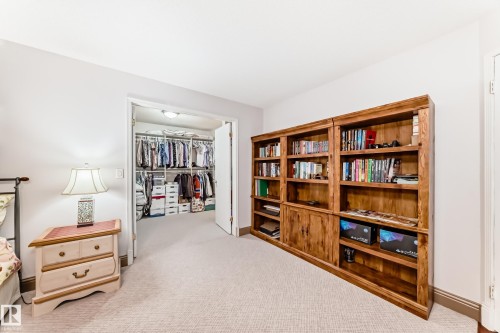 Built-in wooden shelving unit featuring open and closed storage, light-toned carpeting, and a walk-in closet with integrated hanging rods and shelving - 512 3 Perron Street, St. Albert, AB 