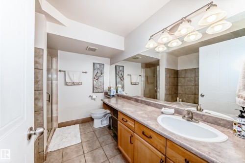 Spacious bathroom featuring a wood-finish vanity with an integrated sink, a full-width mirror, and an overhead vanity light fixture - 512 3 Perron Street, St. Albert, AB 