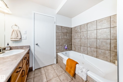 Spacious bathroom featuring a built-in jetted tub with tile surround, a large vanity with an integrated sink and light wood cabinetry, and neutral tile flooring - 512 3 Perron Street, St. Albert, AB 