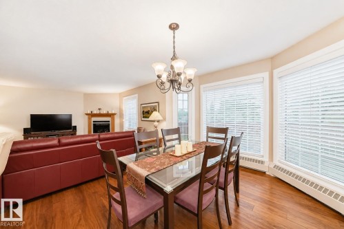 Open-concept living and dining areas featuring wood-finish flooring, a fireplace with a wood mantel, and multiple large windows with blinds - 512 3 Perron Street, St. Albert, AB 