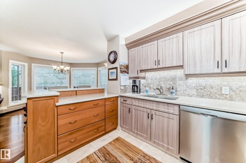 Kitchen featuring light-toned upper cabinetry with dark hardware, a stainless steel sink with a gooseneck faucet, and a stone-patterned backsplash - 512 3 Perron Street, St. Albert, AB 