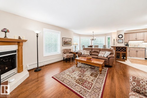 Spacious living area featuring wood-finish flooring, a fireplace with a light-toned hearth and wood mantel, and multiple windows with blinds - 512 3 Perron Street, St. Albert, AB 