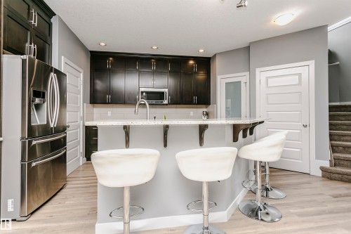 Kitchen featuring dark wood cabinetry, stainless steel appliances, and a light-colored countertop with an extended breakfast bar - 21807 97 Avenue, Edmonton, AB 
