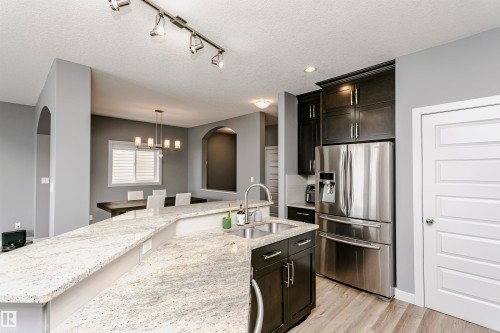 Kitchen featuring a large island with a double basin sink and light-toned countertop, dark cabinetry, and stainless steel appliances - 21807 97 Avenue, Edmonton, AB 