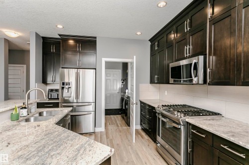 Modern kitchen featuring dark wood-finish cabinetry with brushed nickel hardware, light-toned granite countertops, and stainless steel appliances - 21807 97 Avenue, Edmonton, AB 