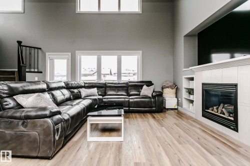 Spacious living area featuring light wood-finish flooring, a white-framed multi-pane window, and a built-in fireplace with a white mantel and integrated shelving - 21807 97 Avenue, Edmonton, AB 