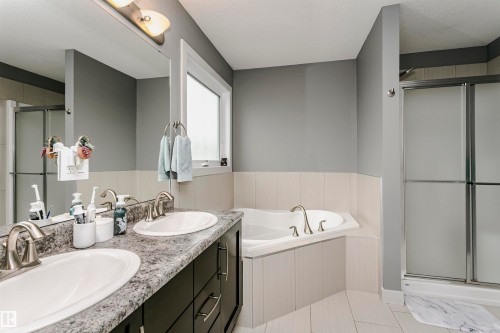 Bathroom featuring a dual vanity with undermount sinks, a built-in corner bathtub, a separate glass-enclosed shower, a large window, and tile flooring - 21807 97 Avenue, Edmonton, AB 