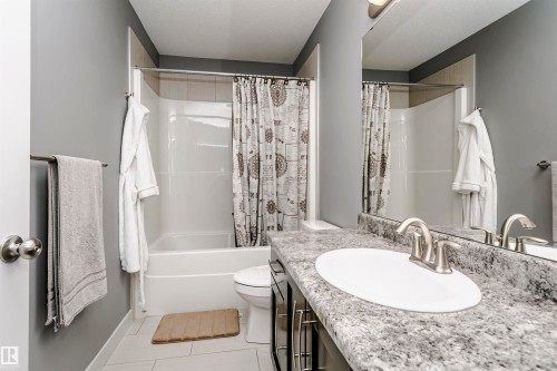 Bathroom featuring a white tub and shower combination, a single vanity with a granite-look countertop, an integrated sink, and brushed nickel fixtures - 21807 97 Avenue, Edmonton, AB 