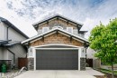 Craftsman-style facade featuring gray siding, natural wood shingles, dark gray garage door, stone pillar accents, and decorative roofline brackets - 21807 97 Avenue, Edmonton, AB 