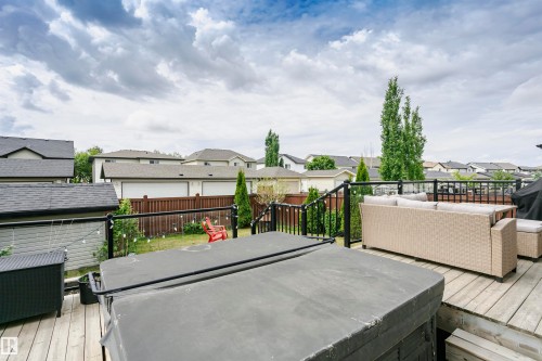 Spacious wood-decked patio featuring a hot tub, clear panel railing, and outdoor furniture - 21807 97 Avenue, Edmonton, AB 