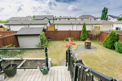 Fenced backyard featuring a gravel fire pit area, a shed with shingle roofing, and a raised garden bed bordering the deck - 21807 97 Avenue, Edmonton, AB 