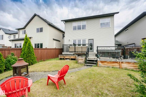 Rear exterior featuring a multi-level deck with glass panel railings, a ground-level patio with wood-framed raised garden beds, a gravel pathway, and mature privacy trees - 21807 97 Avenue, Edmonton, AB 