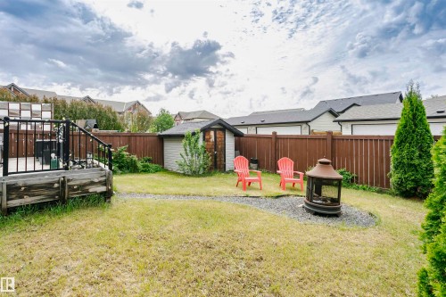 Expansive backyard featuring a central lawn, a gravel patio with a built-in fire pit, a wooden storage shed, and a raised wood planter - 21807 97 Avenue, Edmonton, AB 