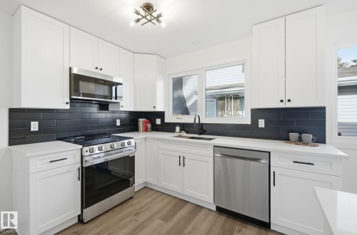 Kitchen with new appliances with stainless steel finishes, white cabinetry, light wood-style floors, black backsplash, and light quartz counters - 2722 104A Street, Edmonton, AB 