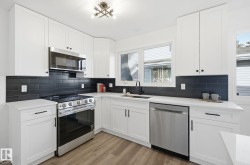 Kitchen with new appliances with stainless steel finishes, white cabinetry, light wood-style floors, black backsplash, and light quartz counters - 