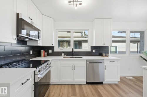 Kitchen featuring new appliances with stainless steel finishes, decorative black backsplash, white cabinets, and plenty of natural light - 2722 104A Street, Edmonton, AB 