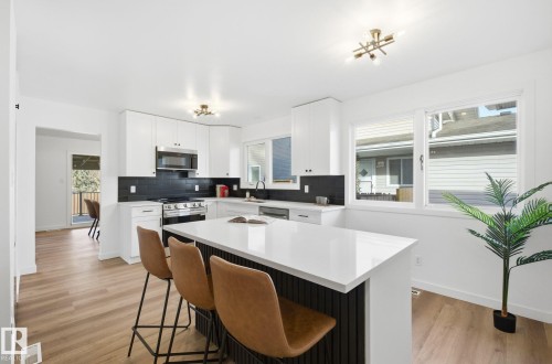 Kitchen with backsplash, white cabinetry, light wood finished floors, stainless steel appliances, and a large island. - 2722 104A Street, Edmonton, AB 