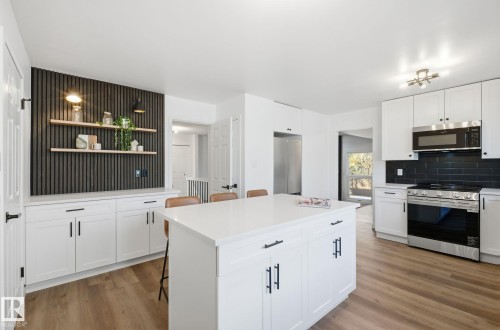Kitchen featuring a kitchen breakfast bar, appliances with stainless steel finishes, white cabinetry, and a kitchen island - 2722 104A Street, Edmonton, AB 