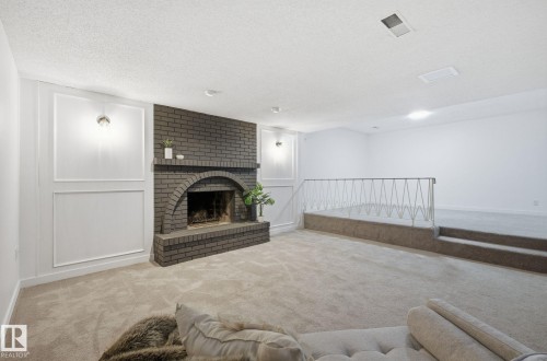Living area with carpet flooring, a decorative wall, a brick fireplace, and a textured ceiling - 2722 104A Street, Edmonton, AB 