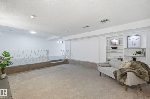 Recreation room featuring carpet, textured ceiling, recessed lighting, two levels, build in shelving units, and a black brick fire place. - 2722 104A Street, Edmonton, AB 