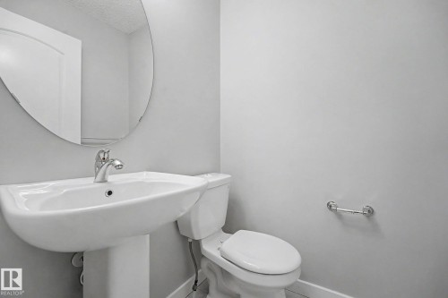Pedestal sink with chrome faucet, oval wall mirror, and toilet featuring chrome hardware - 16810 53 Street, Edmonton, AB 