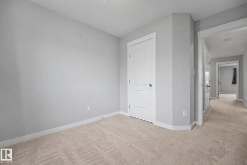 Neutral-toned room featuring light gray walls, white trim, and a textured beige carpet - 16810 53 Street, Edmonton, AB 