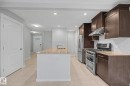 Kitchen featuring a central island with an undermount sink, dark wood cabinetry, stainless steel appliances, neutral tile flooring, and recessed lighting - 16810 53 Street, Edmonton, AB 