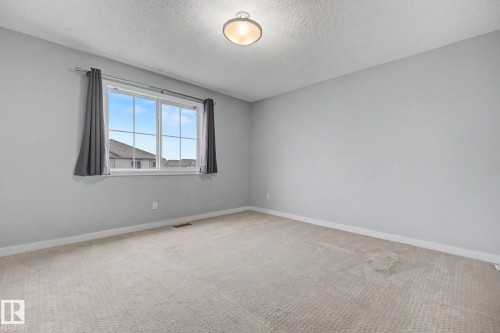 Spacious room featuring neutral carpeting and a large window with vertical grids - 16810 53 Street, Edmonton, AB 