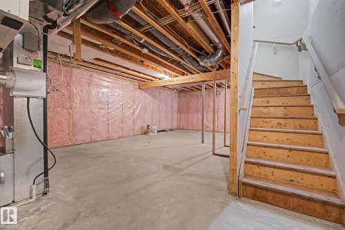 Unfinished basement with concrete flooring, exposed wood beam ceiling, pink insulation, and a utility staircase - 16810 53 Street, Edmonton, AB 