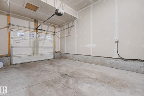 Garage space featuring a concrete floor with a floor drain, an automatic garage door opener, and a panel-style garage door with upper window inserts - 16810 53 Street, Edmonton, AB 