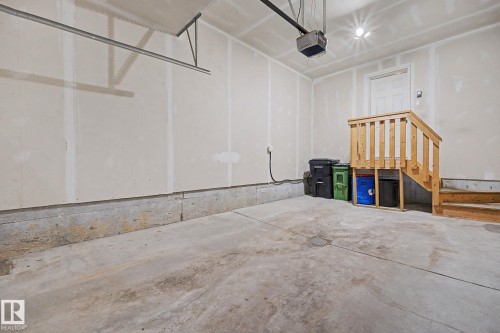 Attached two-car garage featuring a concrete floor, light-toned walls, and a built-in wooden staircase with storage underneath - 16810 53 Street, Edmonton, AB 