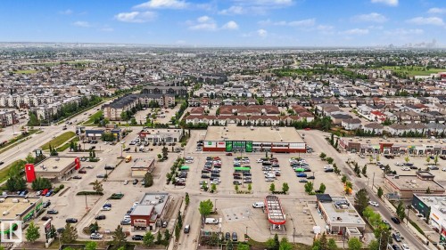 Expansive aerial capturing a suburban landscape featuring a prominent retail center, residential developments, a major roadway, and distant city skyline - 16810 53 Street, Edmonton, AB 