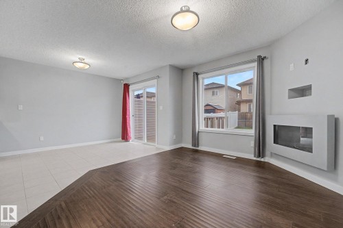 Living area featuring a modern wall-mounted fireplace, a prominent window with grey drapes, and a glass sliding door - 16810 53 Street, Edmonton, AB 