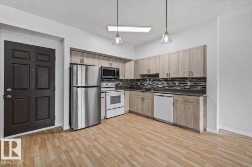 Kitchen featuring wood-finish flooring, light wood-look cabinetry, stainless steel refrigerator, white range, and white dishwasher - 116 6315 135 Avenue, Edmonton, AB 